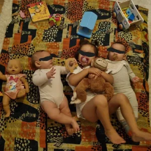 Drei Babys liegen auf einer bunten Decke, spielen.