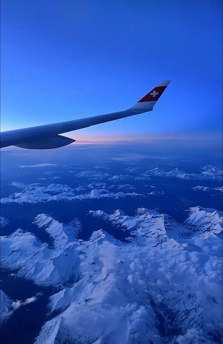 Flugzeugflügel über verschneiten Alpen bei Sonnenuntergang