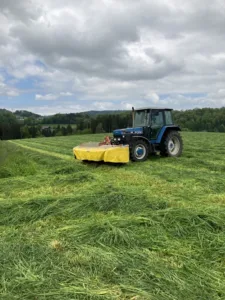 Blauer Traktor mäht grünes Gras auf der Wiese.